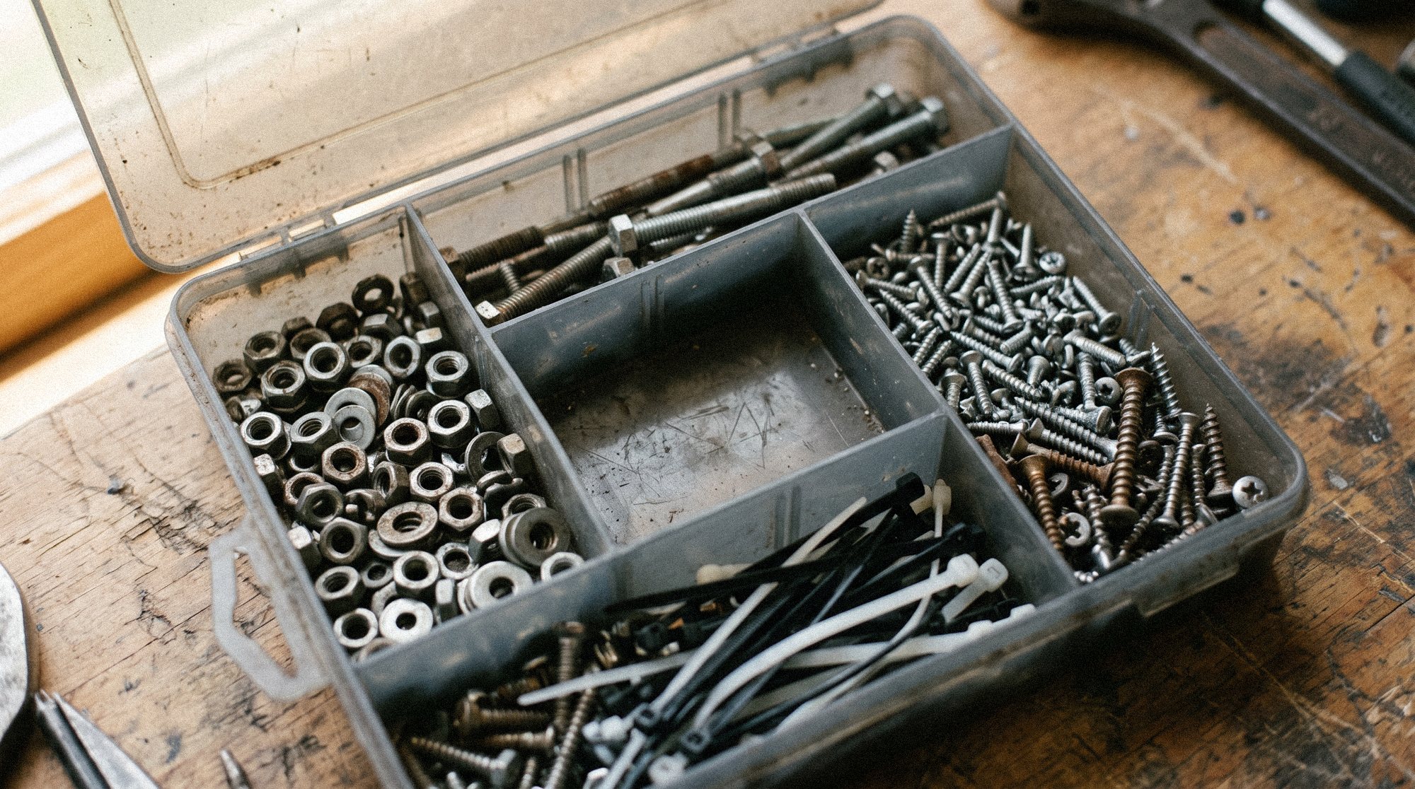 Assortment box with screws, nuts and cable ties, one compartment empty and labelled with a reorder note